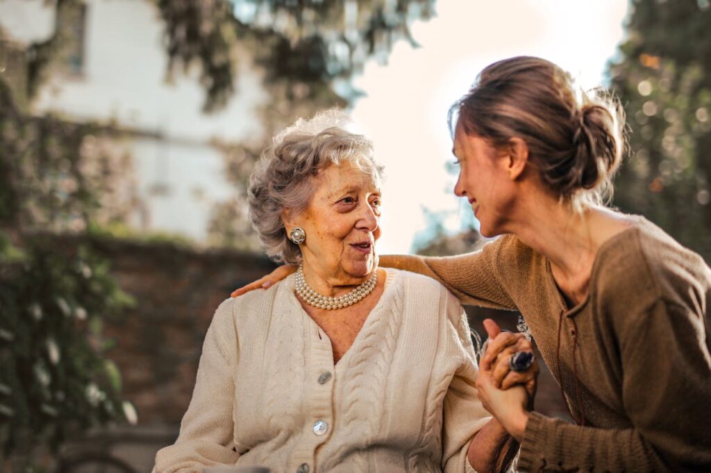SEITEN Elderly woman and adult daughter share a joyful, affectionate moment in a sunny garden.